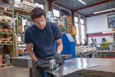 A person wearing safety equipment cuts sheet metal with a cordless metal shear.