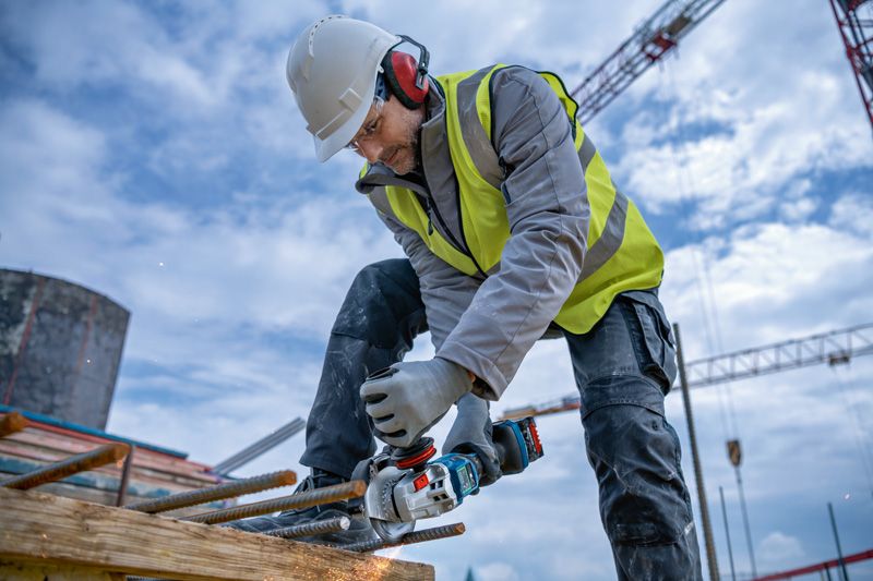 A person wearing safety equipment grinds rebar with a power tool at a construction site.