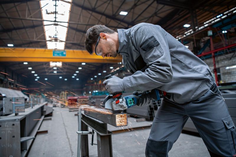 A worker wearing safety equipment grinds metal in an industrial workshop.