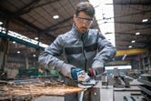 A person wearing safety equipment grinds metal, producing sparks in an industrial workshop.
