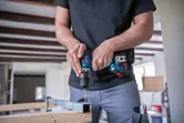 A person drills into a metal beam using a cordless driver inside a workshop.