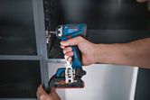 A person uses a cordless drill/driver to fasten a cabinet hinge.