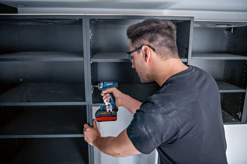 Person wearing safety equipment assembles shelving with a cordless drill or driver.