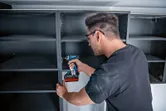 Person wearing safety equipment assembles shelving with a cordless drill or driver.