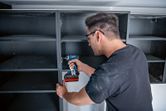Person wearing safety equipment assembles shelving with a cordless drill or driver.
