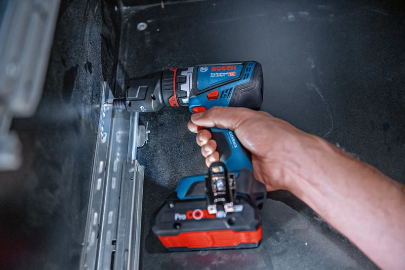 Person using a cordless drill driver to fasten a screw into a metal rail.