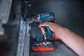 Person using a cordless drill driver to fasten a screw into a metal rail.