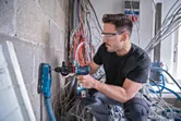 A person wearing safety equipment drills into a concrete wall with dust extraction.