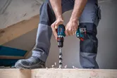 A person wearing safety equipment drills into wood with a cordless drill.