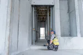 A person wearing safety equipment uses a laser measure to check distance in a concrete structure.