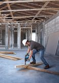 A person wearing safety equipment drills into a wooden beam at a construction site.