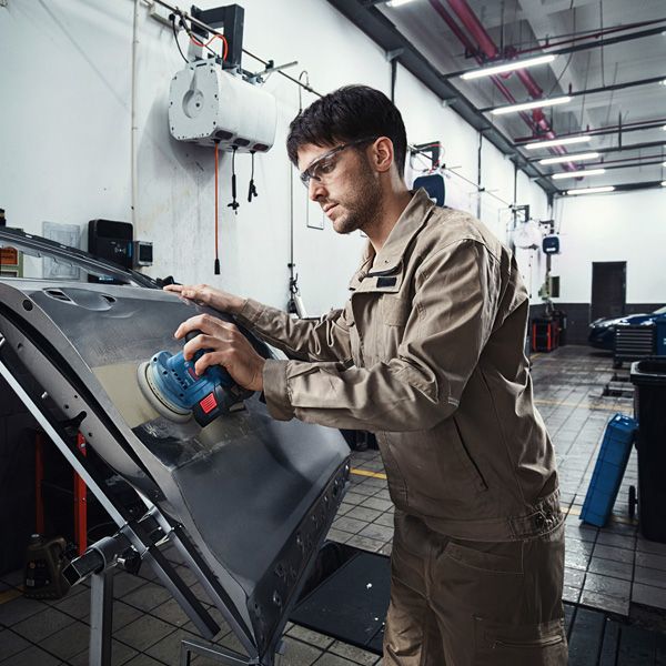 GEX 185-LI A person wearing safety equipment sands a car door with a power sander.