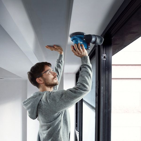 GEX 185-LI A person wearing safety equipment sands a ceiling edge using a power sander.
