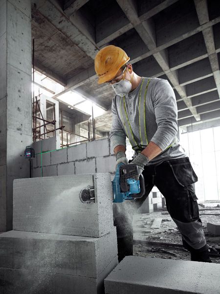 GAC 250 A person wearing safety equipment cuts an AAC block with a power cutter in a construction site.