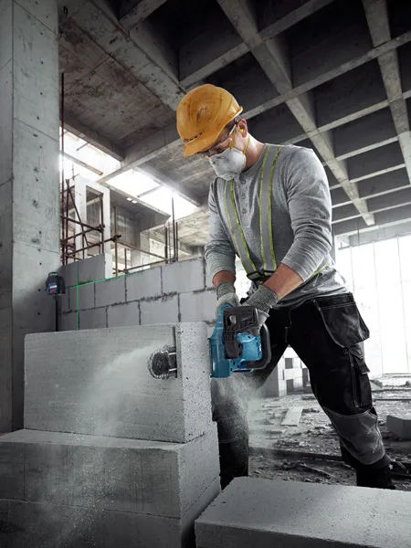 A person wearing safety equipment cuts an AAC block with a power cutter in a construction site.