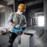 A person wearing safety equipment uses an AAC block cutter on a concrete block.