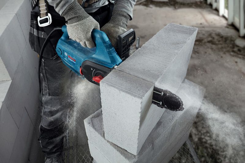 A person wearing safety equipment uses an AAC block cutter to cut through a concrete block.