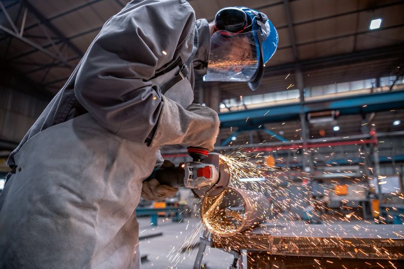 A person wearing safety equipment grinds metal with an angle grinder, producing sparks.
