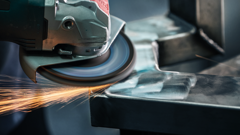 Angle grinder producing sparks while grinding the edge of a metal beam.
