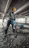 A person wearing safety equipment uses a breaker to demolish concrete flooring.