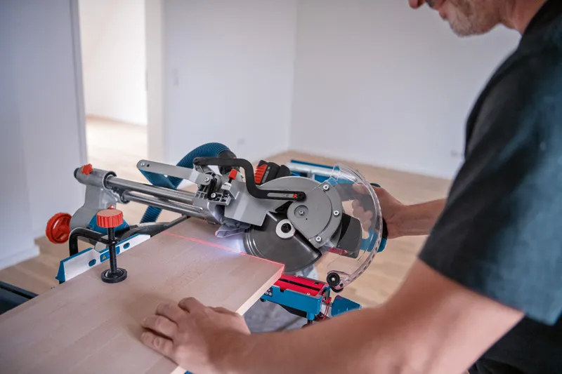 A person uses a cordless mitre saw with a laser leveling tool to cut wood.