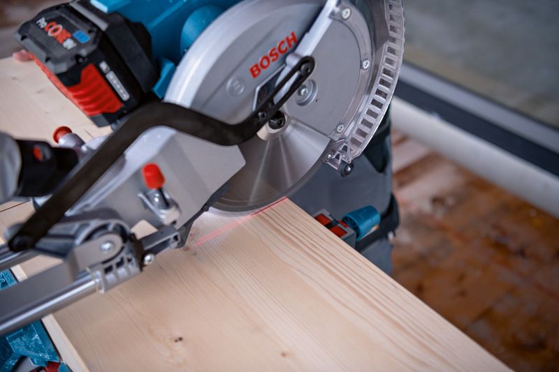 Cordless mitre saw uses a laser leveling tool to guide a straight cut on wood.
