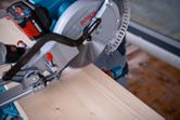 Cordless mitre saw uses a laser leveling tool to guide a straight cut on wood.
