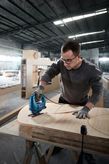 Person wearing safety equipment uses a jigsaw to cut curved shapes in plywood.