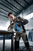 A person wearing safety equipment operates a jigsaw to cut a sheet of metal.