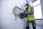 Person wearing safety equipment uses a cordless rotary hammer to break through a tiled wall.
