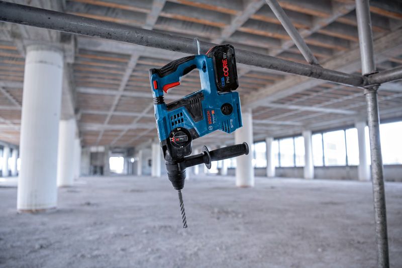 Cordless rotary hammer hanging on a metal pipe at an unfinished construction site.