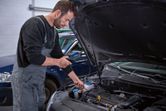 A person in coveralls inspects a car engine bay using an inspection camera.