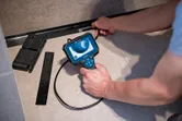 A person inspects a narrow floor space using an inspection camera device.