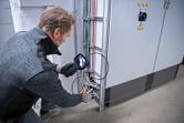 A person wearing safety equipment inspects electrical wiring using an inspection camera.