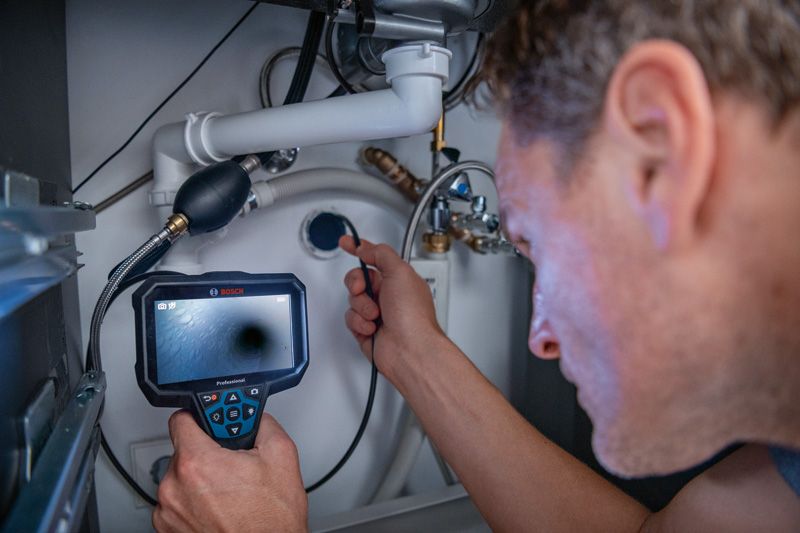 A person inspects pipes under a sink using an inspection camera.