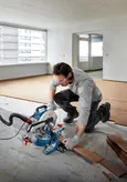 A person wearing safety equipment cuts wooden flooring with a mitre saw.