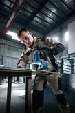 A person wearing safety equipment uses a jigsaw to cut metal in a workshop.