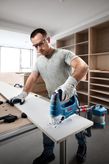 A person wearing safety equipment cuts wood with a jigsaw in a workshop.