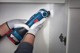 A person wearing safety equipment uses a cordless power tool to cut a cabinet wall.