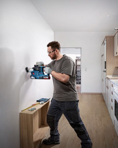 Person wearing safety equipment drills into a wall near a measuring tool and screws.