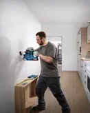 Person wearing safety equipment drills into a wall near a measuring tool and screws.