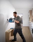 Person wearing safety equipment drills into a wall near a measuring tool and screws.