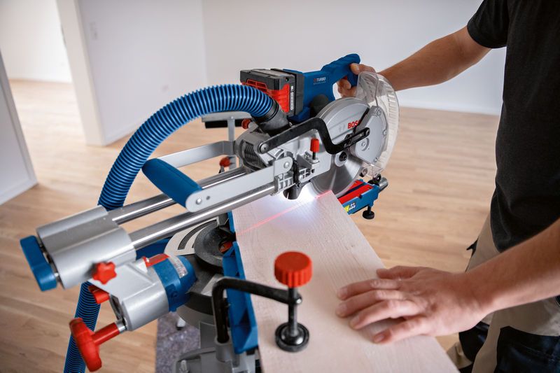 A person operates a cordless mitre saw cutting wood guided by a laser leveling tool.