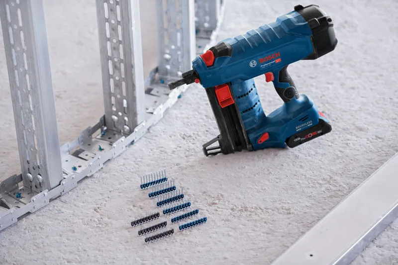 Cordless concrete nailer placed on a construction site floor beside metal framing and fasteners.