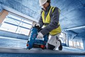 A person wearing safety equipment uses a cordless concrete nailer on a construction floor.