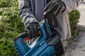 A person wearing safety equipment inserts a battery into a cordless leaf blower outdoors.