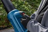 A person wearing safety equipment operates a cordless leaf blower outdoors.