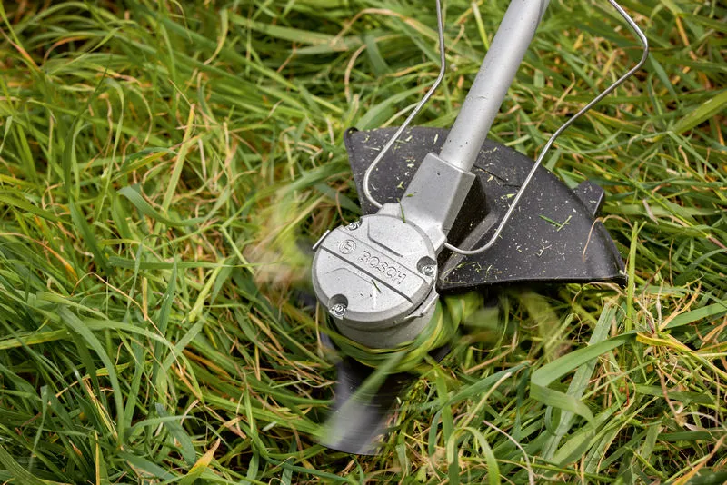 Cordless brushcutter trims tall grass with spinning blade.