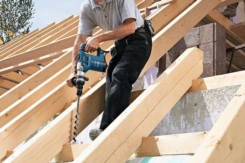 GBH 4-32 DFR A person drilling into a wooden beam on a roof structure, not wearing safety equipment.