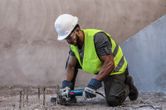 A person wearing safety equipment cuts exposed rebar with an angle grinder.